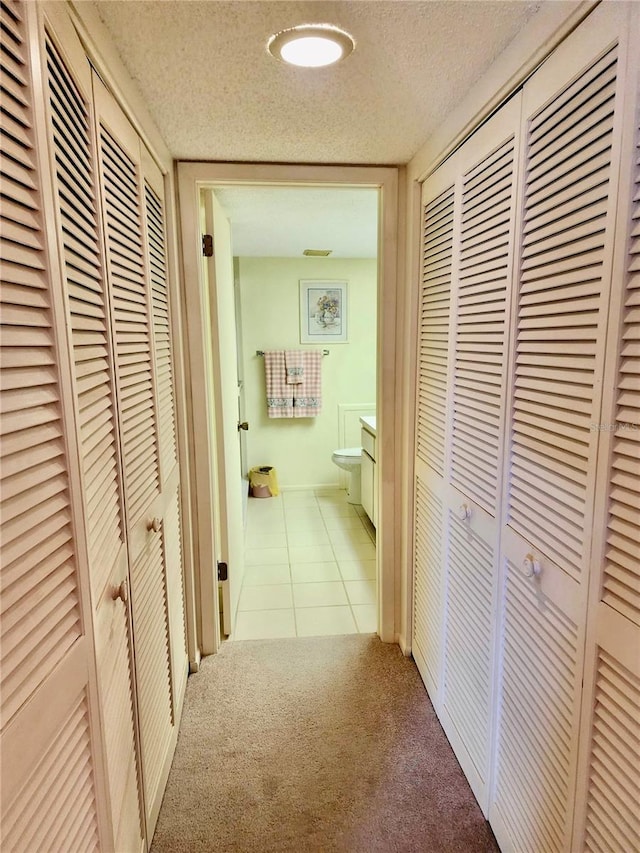 corridor with light colored carpet and a textured ceiling