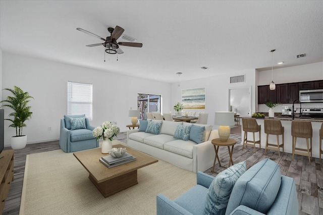 living room with ceiling fan, sink, and light wood-type flooring