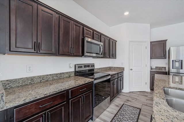 kitchen with light stone countertops, appliances with stainless steel finishes, sink, and dark brown cabinetry