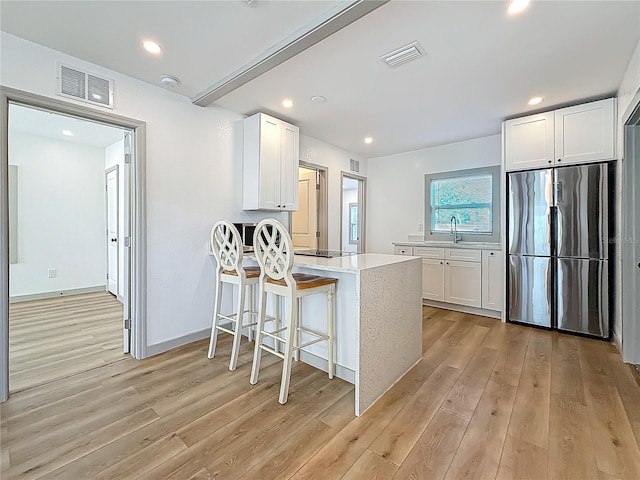 kitchen with white cabinetry, stainless steel fridge, a kitchen bar, and light hardwood / wood-style flooring