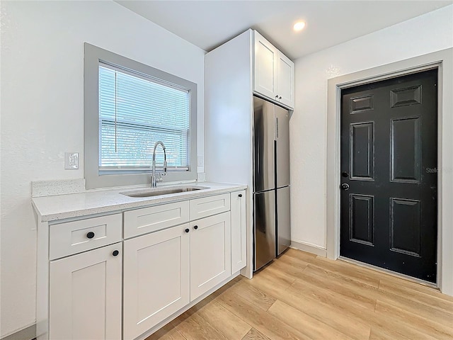 kitchen featuring white cabinetry, sink, stainless steel refrigerator, and light wood-type flooring