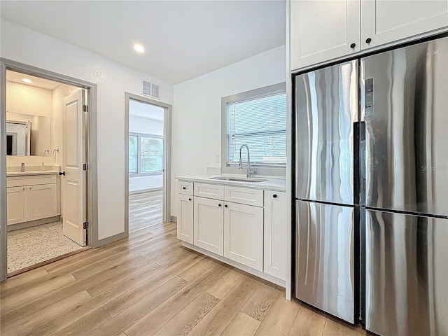 kitchen with sink, white cabinets, stainless steel refrigerator, and light wood-type flooring