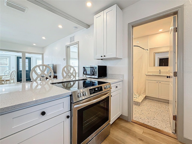 kitchen featuring white cabinetry, appliances with stainless steel finishes, beamed ceiling, light stone countertops, and light hardwood / wood-style floors