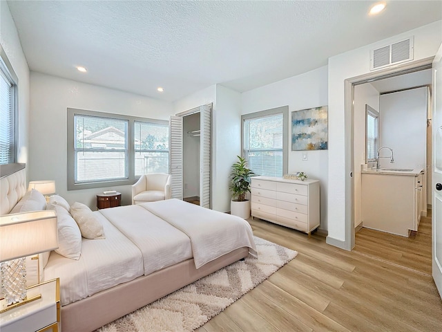 bedroom with sink, a textured ceiling, and light hardwood / wood-style flooring