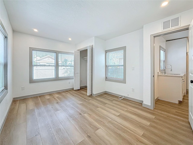 unfurnished bedroom with sink, a textured ceiling, light hardwood / wood-style floors, and a closet