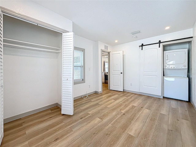 unfurnished bedroom with a closet, stacked washer and clothes dryer, a barn door, and light hardwood / wood-style flooring