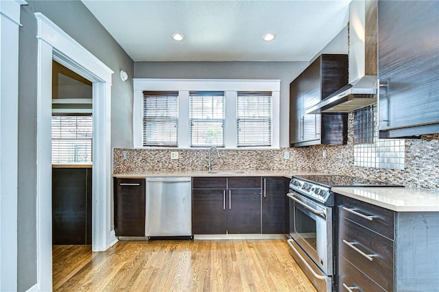 kitchen with appliances with stainless steel finishes, tasteful backsplash, sink, light hardwood / wood-style floors, and wall chimney exhaust hood