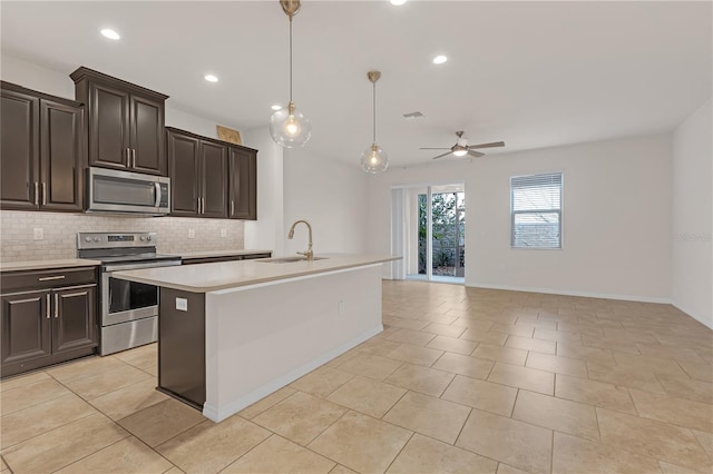 kitchen with appliances with stainless steel finishes, decorative light fixtures, tasteful backsplash, sink, and a center island with sink