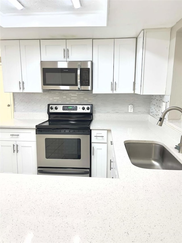 kitchen featuring sink, appliances with stainless steel finishes, white cabinets, light stone countertops, and backsplash