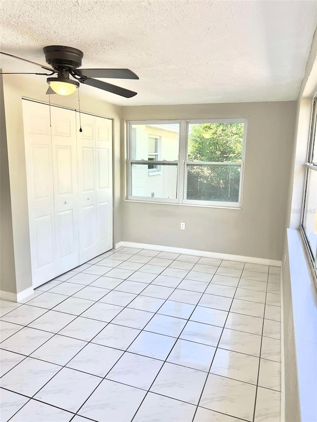 unfurnished bedroom featuring light tile patterned flooring, ceiling fan, a closet, and a textured ceiling