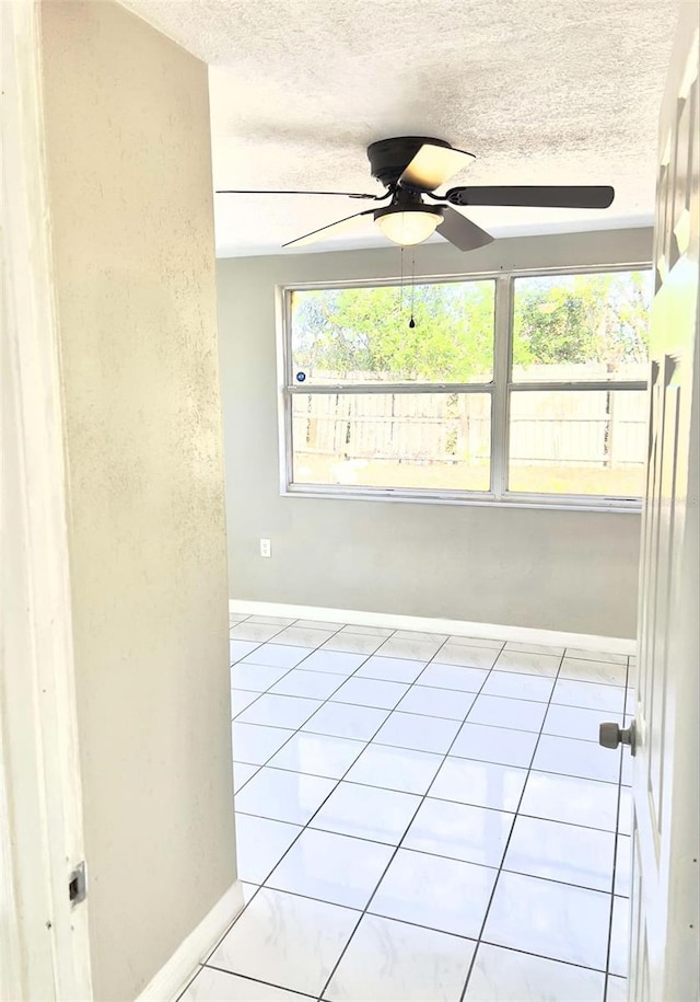 spare room featuring ceiling fan, light tile patterned floors, and a textured ceiling