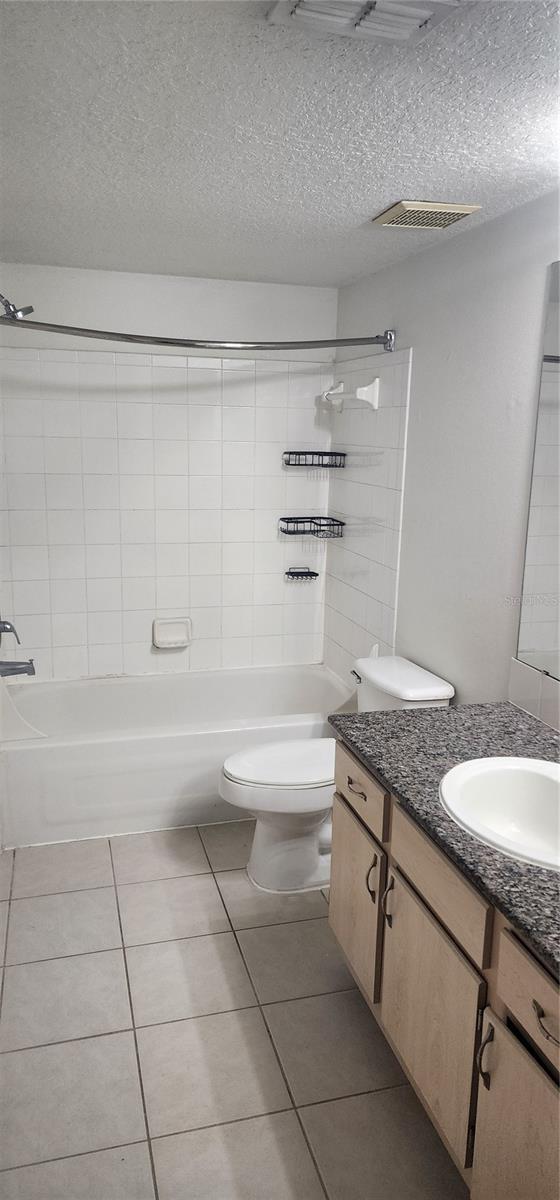 full bathroom with tiled shower / bath, tile patterned flooring, vanity, toilet, and a textured ceiling