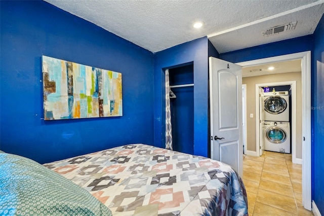 tiled bedroom with a closet, stacked washer and clothes dryer, and a textured ceiling