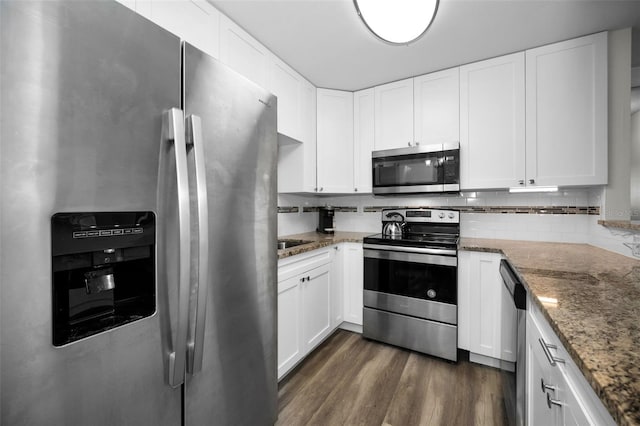 kitchen with appliances with stainless steel finishes, dark stone countertops, white cabinets, and dark hardwood / wood-style flooring