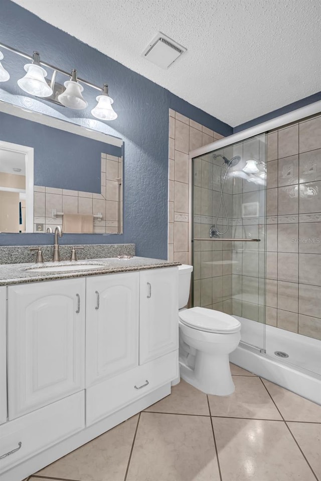 bathroom with toilet, a textured ceiling, vanity, a shower with door, and tile patterned flooring