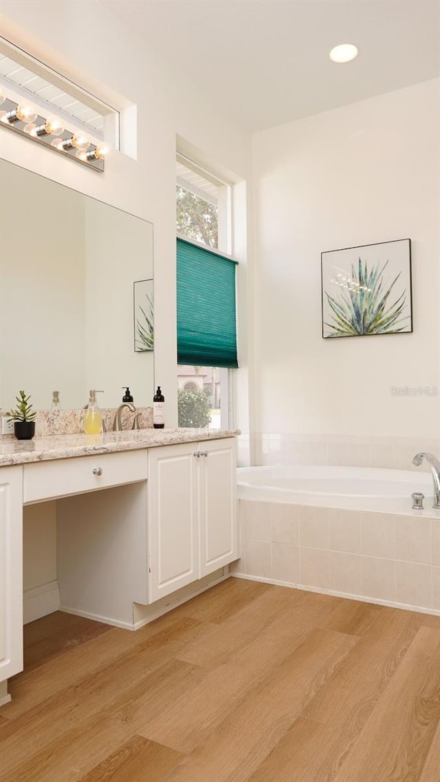 bathroom featuring tiled tub, wood-type flooring, and vanity