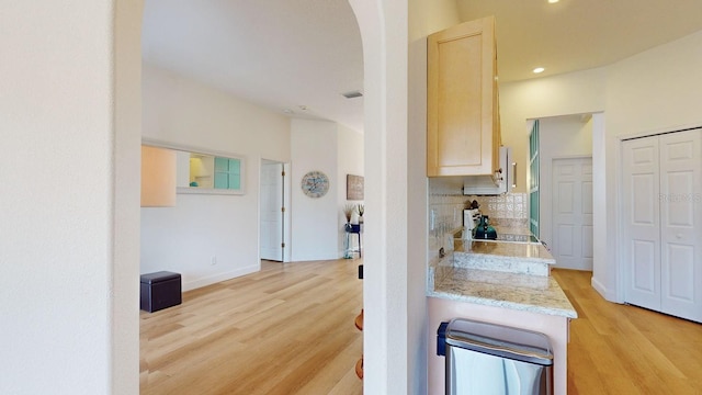 kitchen with light stone countertops, light hardwood / wood-style floors, light brown cabinets, and backsplash