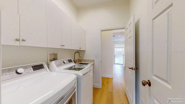 clothes washing area with cabinets, sink, washer and dryer, and light wood-type flooring