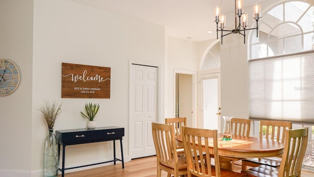 dining area with a towering ceiling, an inviting chandelier, and light hardwood / wood-style flooring