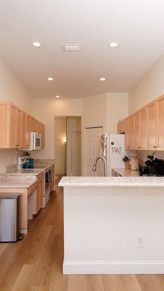 kitchen featuring stainless steel electric range oven, light hardwood / wood-style flooring, light brown cabinets, white fridge, and backsplash