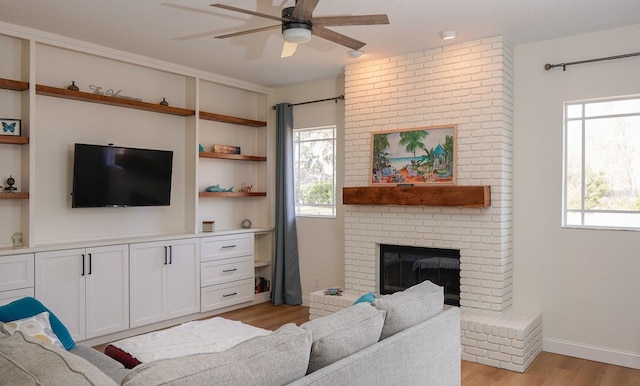 living room with a brick fireplace, a wealth of natural light, ceiling fan, and light wood-type flooring