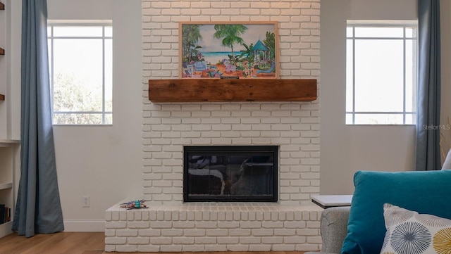 living room featuring a healthy amount of sunlight, light hardwood / wood-style floors, and a brick fireplace