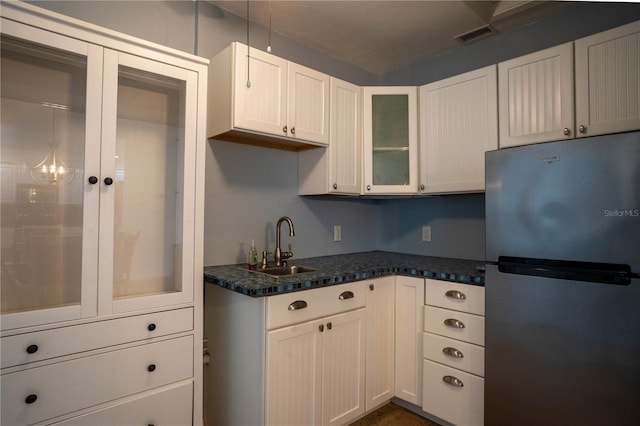 kitchen with dark stone counters, stainless steel fridge, sink, and white cabinets