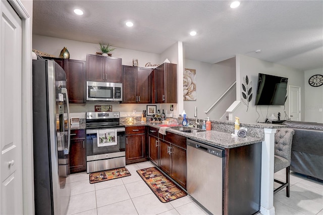 kitchen featuring appliances with stainless steel finishes, sink, a breakfast bar area, light tile patterned floors, and light stone countertops