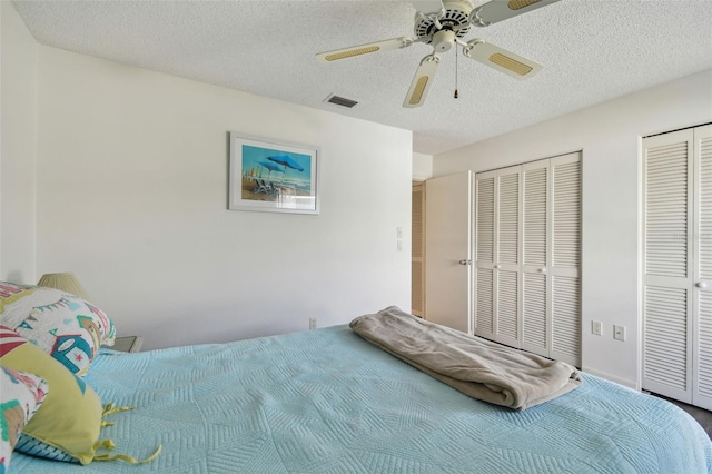 bedroom with ceiling fan, two closets, and a textured ceiling