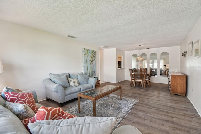 living room with dark hardwood / wood-style flooring, a textured ceiling, and an inviting chandelier