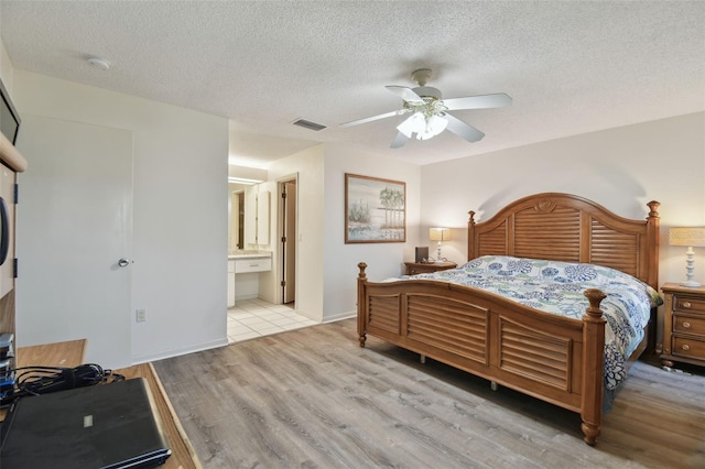 bedroom featuring ceiling fan, ensuite bath, light hardwood / wood-style floors, and a textured ceiling