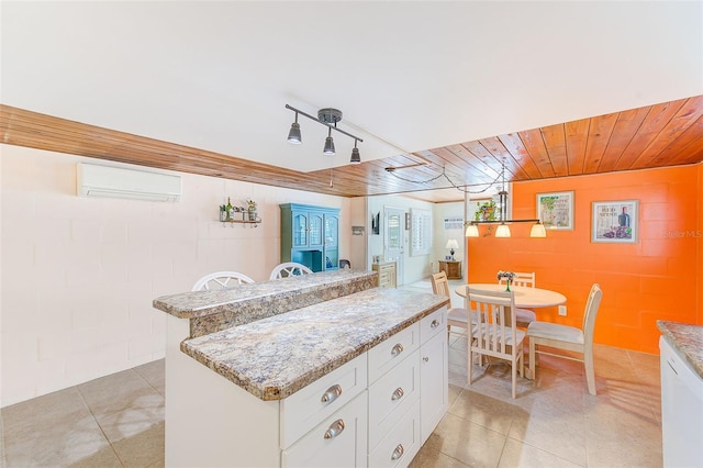 kitchen featuring light stone counters, a wall mounted air conditioner, a center island, and white cabinets