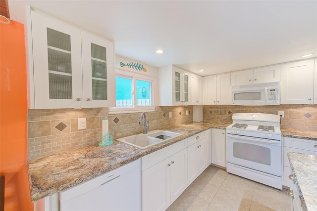 kitchen with tasteful backsplash, sink, white cabinets, light tile patterned floors, and white appliances