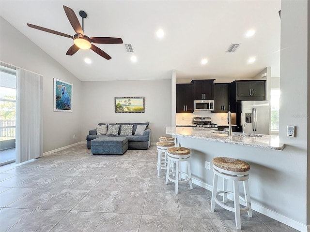 kitchen with sink, a kitchen bar, kitchen peninsula, stainless steel appliances, and light stone countertops