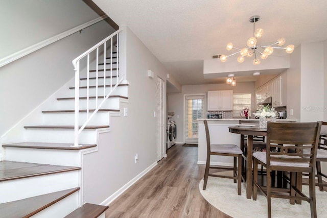 dining room with a notable chandelier, light hardwood / wood-style flooring, washer and dryer, and a textured ceiling