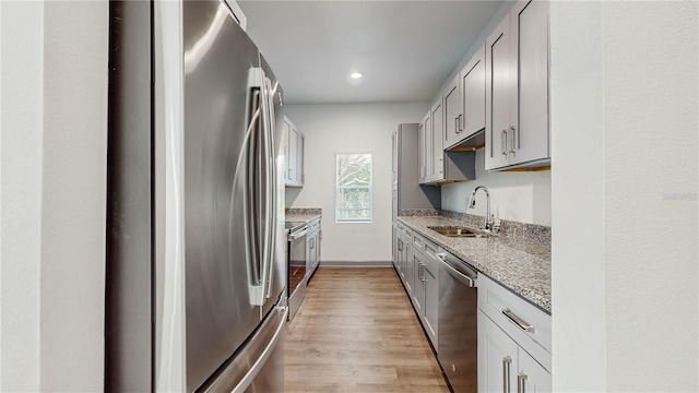 kitchen with sink, light wood-type flooring, appliances with stainless steel finishes, gray cabinets, and light stone countertops