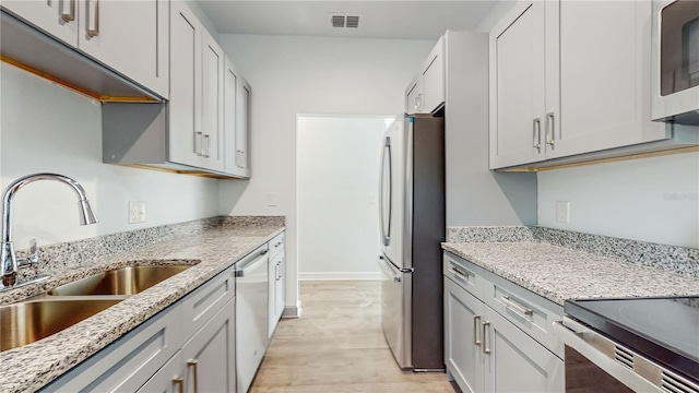 kitchen with light stone counters, appliances with stainless steel finishes, sink, and light wood-type flooring