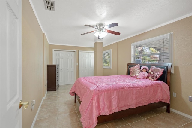 tiled bedroom featuring ceiling fan, ornamental molding, and multiple closets