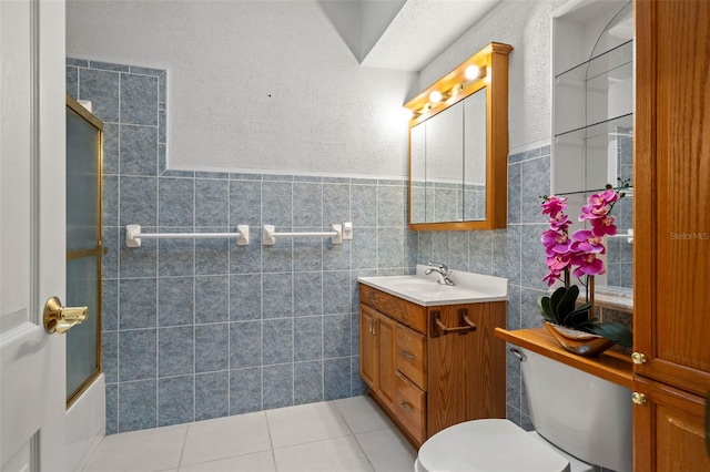 full bathroom featuring tile patterned floors, toilet, shower / bath combination with glass door, tile walls, and vanity