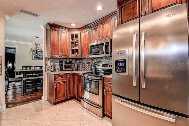 kitchen with light tile patterned floors, appliances with stainless steel finishes, backsplash, light stone counters, and ornamental molding