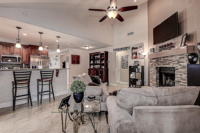 living room featuring crown molding, ceiling fan, a fireplace, and a high ceiling