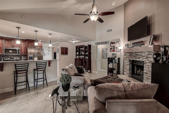 living room with ceiling fan, a towering ceiling, crown molding, and a fireplace