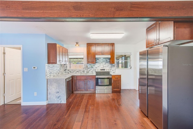 kitchen featuring dark wood-style flooring, stainless steel appliances, decorative backsplash, light countertops, and under cabinet range hood