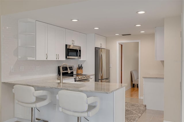 kitchen featuring a breakfast bar, white cabinetry, light stone counters, kitchen peninsula, and stainless steel appliances