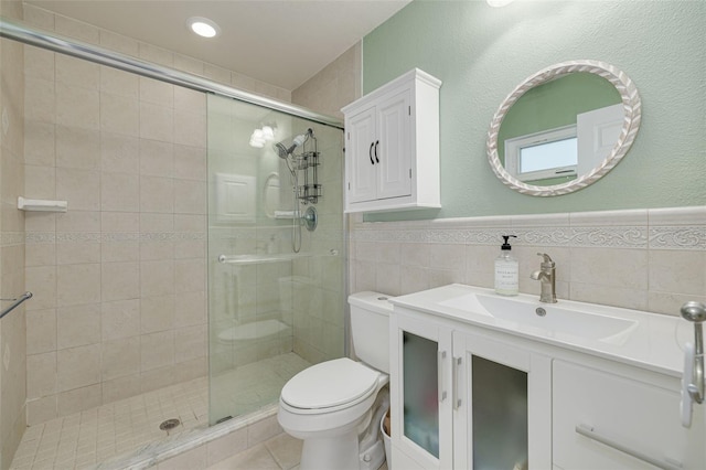 bathroom featuring a shower with door, tile patterned flooring, tile walls, vanity, and toilet