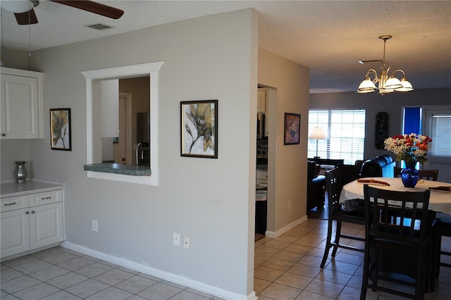 tiled dining area with ceiling fan with notable chandelier and a textured ceiling