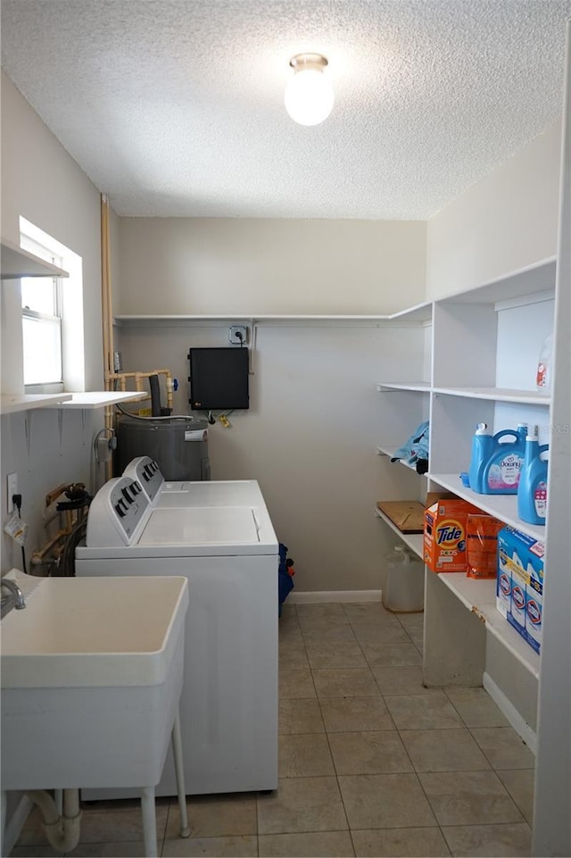 clothes washing area featuring sink, tile patterned flooring, washing machine and clothes dryer, electric water heater, and a textured ceiling