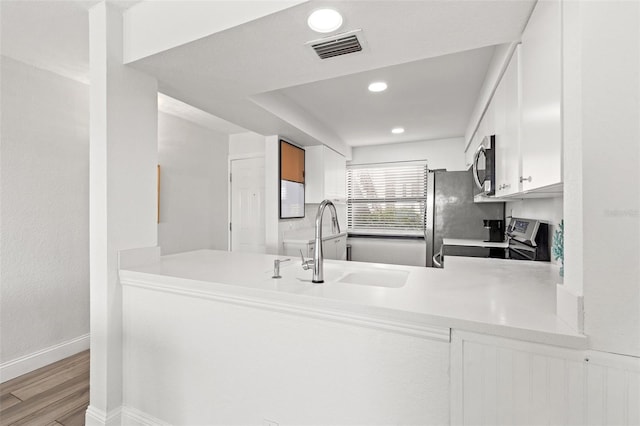 kitchen with sink, white cabinets, kitchen peninsula, stainless steel appliances, and light wood-type flooring