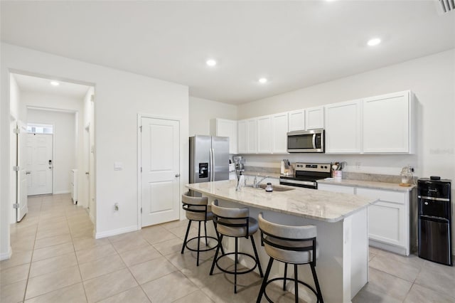 kitchen featuring white cabinetry, appliances with stainless steel finishes, light stone counters, and a center island with sink