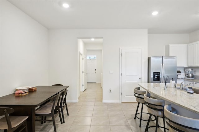 kitchen with light tile patterned flooring, sink, white cabinets, stainless steel fridge, and light stone countertops